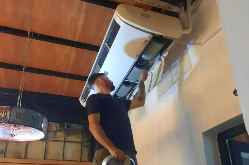 Técnico sobre una escalera trabajando en un equipo piso-techo abierto en un local comercial